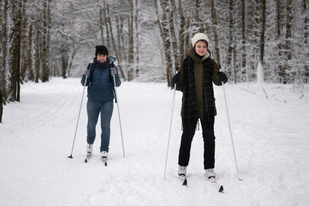 Teenage girl with her mother is skiing in the Moscow park in winter