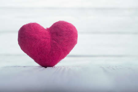Pink woolen heart on white textured wooden boards with white boards on the backgroundの写真素材