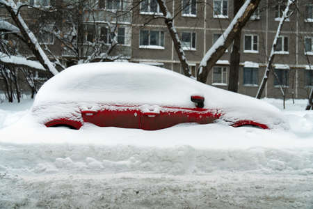 Red car stands in a deep snowdrift after a hard snowstorm in winterの写真素材