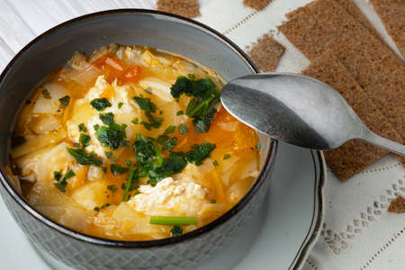 Bowl of a tasty hot soup with chicken meatballs and a spoon and rye crispbreadsの写真素材