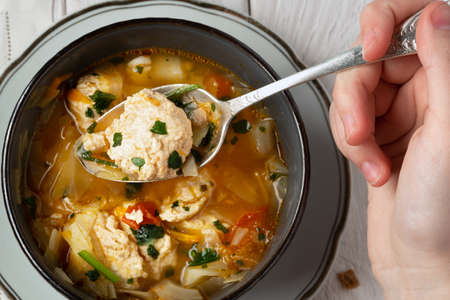 Close-Up of a young girl's hand holding in the spoon a chicken meatball during eating a soup. View from above.の写真素材