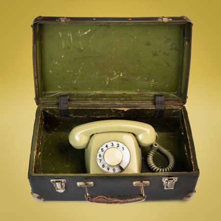 Retro dial phone in an old suitcase isolated on the yellow backgroundの写真素材