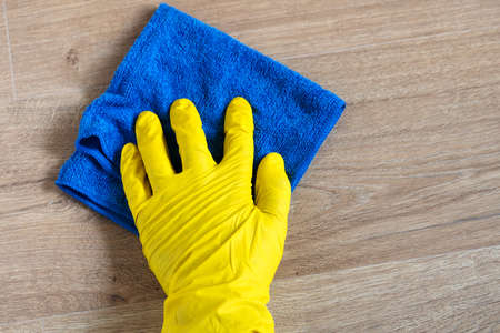 Hand in a rubber glove washing a laminate flooring with a wet cloth