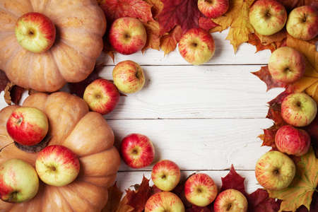 Background with pumpkins, apples, fallen maple leaves on the white wooden boards