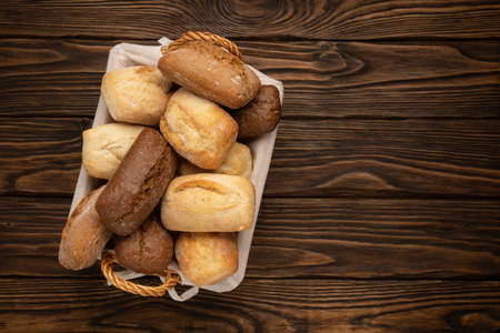 Fresh wheat and rye bread in a wicker basket on a brown wooden tableの写真素材