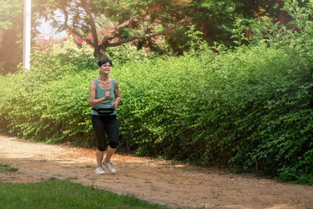 Middle aged woman running in the park in summer morning