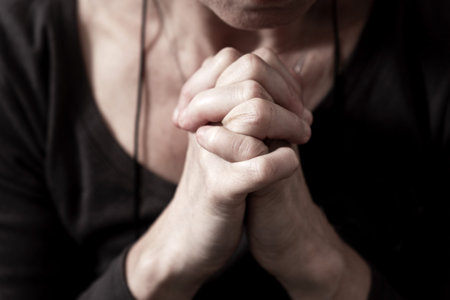 Womans hands folded under her chin in a gesture of anxious anticipation, worry, reflection, or...