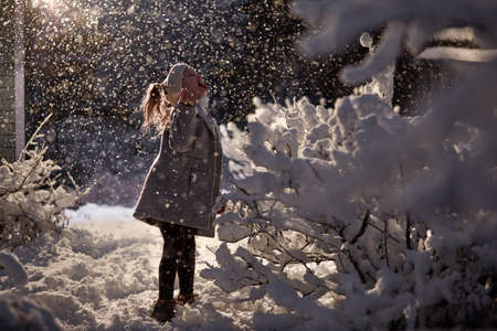 girl in snow catches snowflakes under a lantern