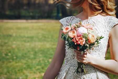 Bride in Wedding Dress with Wedding Bouquet in Hand in the Parkの写真素材