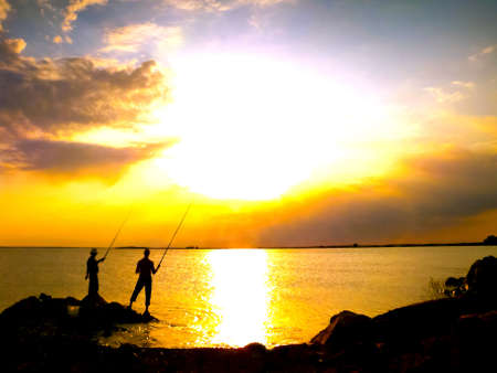 Silhouette, bright sunset two men fish at the sea の写真素材
