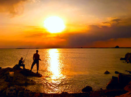 Coastline, beautiful sunset two men fish at the sea.の写真素材