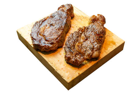 2 prime ribeyes cooked in medium rare on a wooden board white backgroundの写真素材