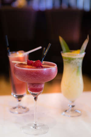 Strawberry daiquiri and pina colada cocktails garnished with raspberry and pineapple leaves. Situated on a marble table at a barの写真素材
