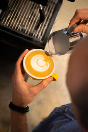 Latte art being made by a barista into a yellow coffee cup at a coffee shopの写真素材