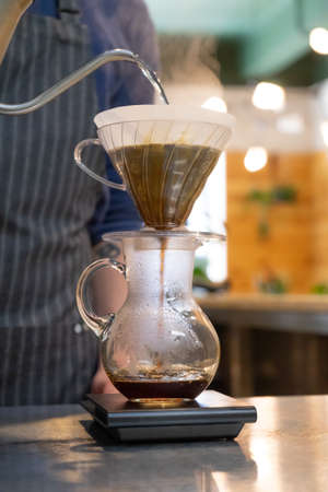 See steam rising from a barista pouring hot water to make filtered coffee at a cafe