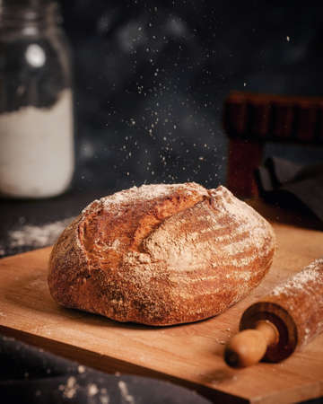 Sourdough bread on a chopping board with dusted flour and rolling pin. View at a table with a dark backgroundの写真素材