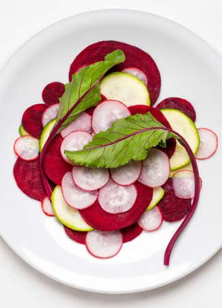 Beetroot Leaves on layered thin slices of Beetroot, Radish and Courgette on a white plate and white backgroundの写真素材