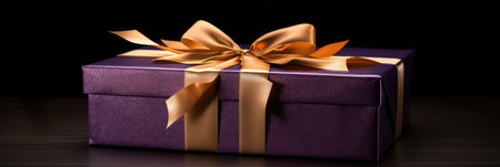 Purple gift box with golden bow on black background.の素材