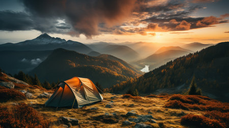Camping in the mountains at sunset. The tent stands on a grassy hilltop against the backdrop of a beautiful mountain landscape.の素材