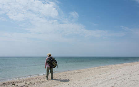 A lonely tourist with a backpack stands and waits on a deserted deserted beach of the sea or oceanの写真素材