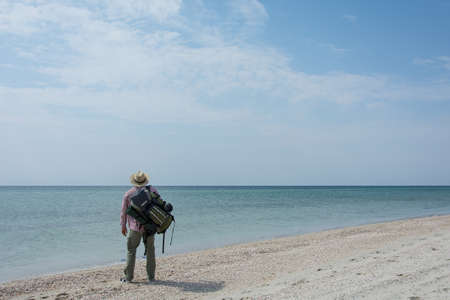 A lonely tourist with a backpack stands and waits on a deserted deserted beach of the sea or oceanの写真素材