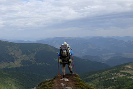 A lone tourist in a hat and with a backpack stands on the edge of a rock and looks into the distanceの写真素材