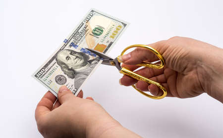Hands of a woman with scissors cut a hundred American dollars