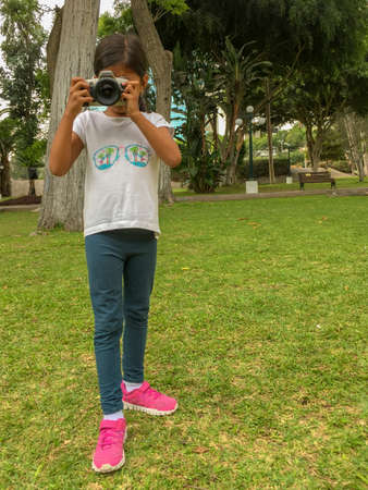Cute little girl playing with real camera in the parkの写真素材