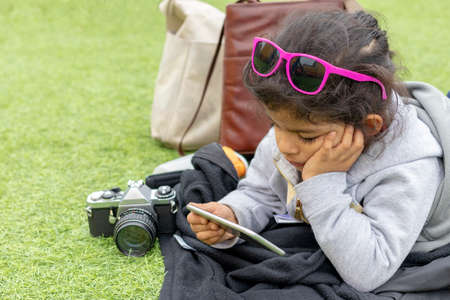 Cute little girl with sunglass checking her smartphone while restingの写真素材