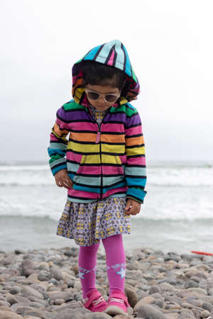 Cute little girl with colorful sweater walking on the beachの写真素材