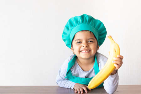 Cute little girl cook playing with a banana, as if it were a phoneの写真素材