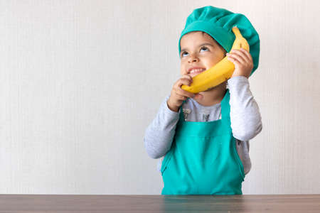 Cute little girl cook playing with a banana, as if it were a phoneの写真素材