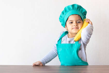 Cute little girl cook playing with a banana, as if it were a phoneの写真素材
