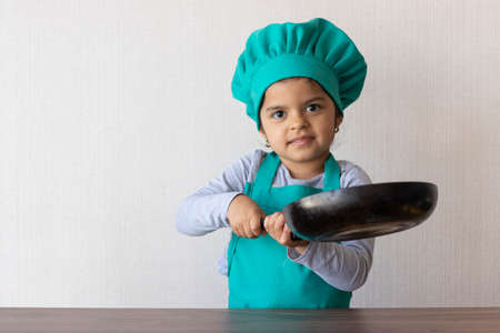 Cute little girl cooking with her frying pan in the kitchenの写真素材