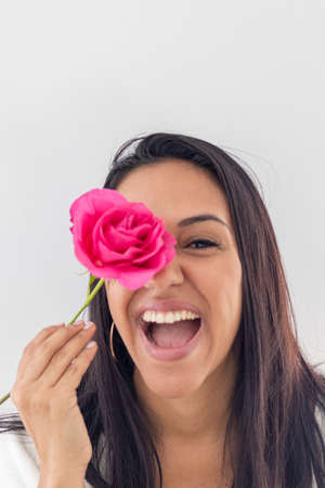 Cute smiling brunette playing with a red roseの写真素材