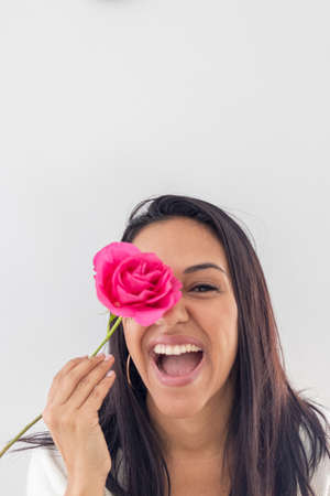 Cute smiling brunette playing with a red roseの写真素材
