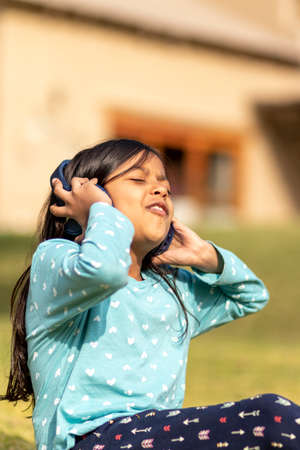 Little girl listening to music on the smartphone with her headphones in the parkの写真素材