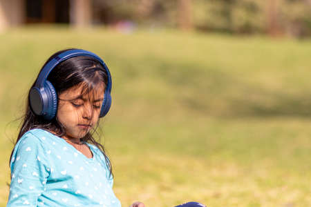 Little girl listening to music on the smartphone with her headphones in the parkの写真素材