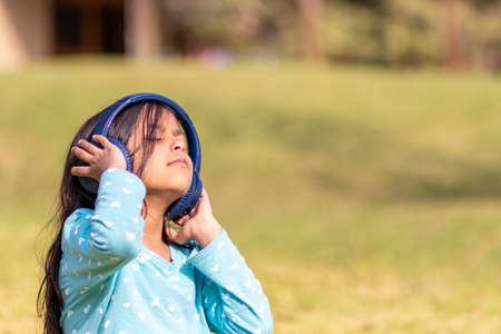 Little girl listening to music on the smartphone with her headphones in the parkの写真素材
