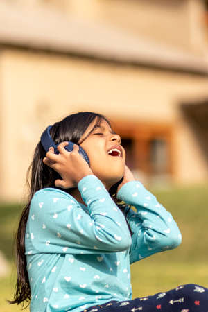 Little girl listening to music on the smartphone with her headphones in the parkの写真素材