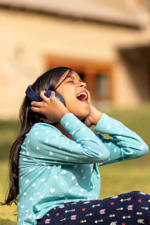 Little girl listening to music on the smartphone with her headphones in the parkの写真素材