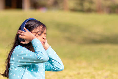 Little girl listening to music on the smartphone with her headphones in the parkの写真素材