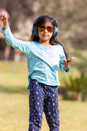 Little girl listening to music on the smartphone with her headphones in the parkの写真素材