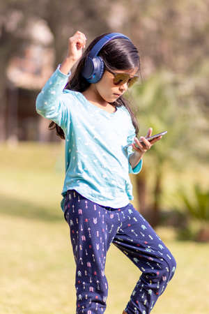 Little girl listening to music on the smartphone with her headphones in the parkの写真素材