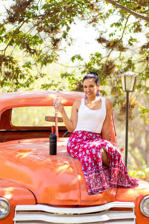 Latin brunette woman next to a bottle of wine on a classic carの写真素材