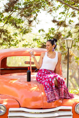 Latin brunette woman next to a bottle of wine on a classic carの写真素材