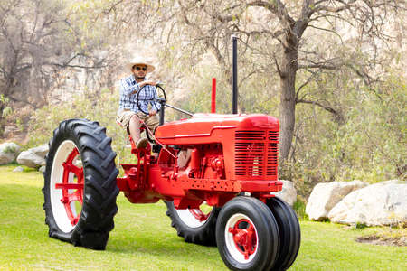 Handsome man with sunglasses driving the tractor to work on the farmの写真素材
