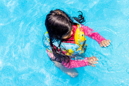 Little girl swimming with floaties, in the blue waters of a pool in the summerの写真素材