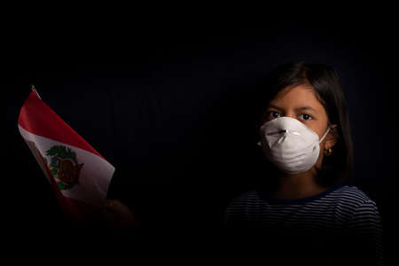 Portrait of little Peruvian girl wearing medical mask and holding hopefully the flag of Peruの写真素材