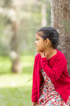 Little girl in flower dress and red sweater, very happy and smiling in the forestの写真素材